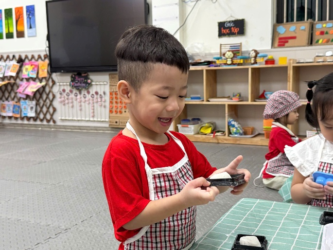A child in a red shirt and apron holding a small object
AI-generated content may be incorrect.
